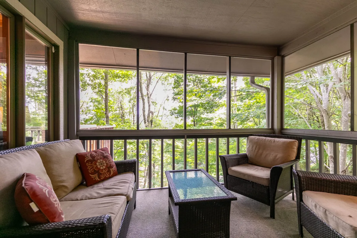 A bright and airy seating area with woven furniture and decorative cushions, set against expansive windows framing lush green views. The relaxed groupings invite guests to unwind, socialize, or gaze out at the surrounding landscape after a day of exploring the local towns.