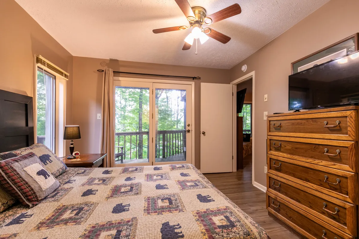 A serene bedroom with a bed, dresser, and a sliding glass door opening to a private balcony or porch. A lamp beside the bed adds to the coziness, while the sliding door hints at direct outdoor access and views.