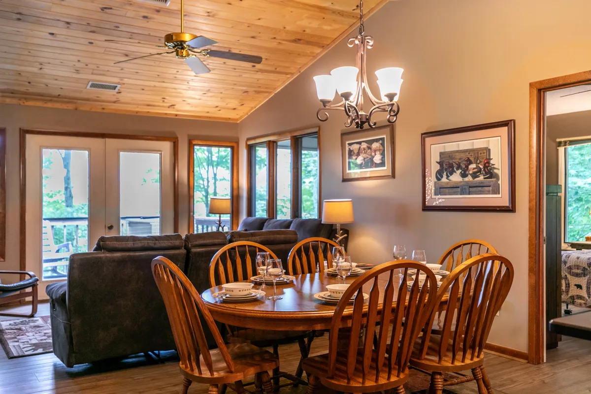 The image captures a dining area set for a meal, adjacent to a comfortable seating nook. Large windows allow in plenty of natural light and frame stunning outdoor views. The space is styled to encourage both family dinners and casual gatherings, with a sense of openness and togetherness.