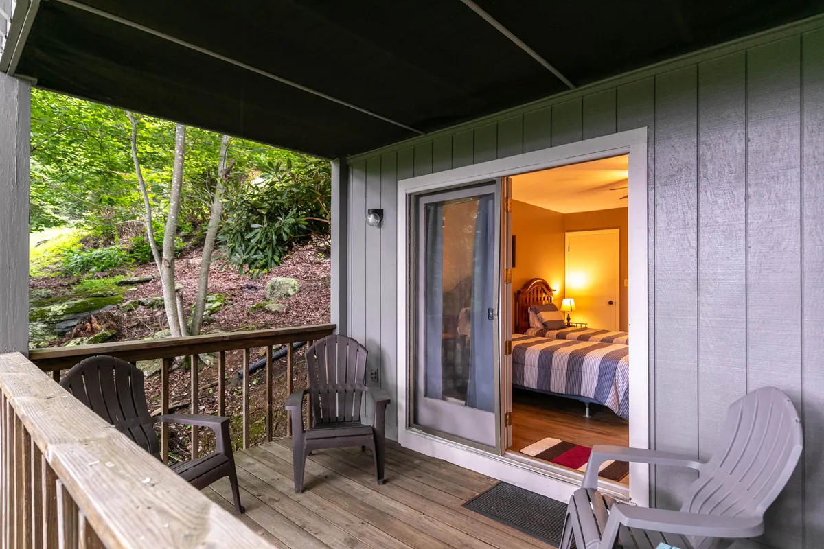 This inviting scene features patio chairs on a private porch with the open door offering a glimpse into the bedroom beyond. Surrounded by lush greenery, it perfectly showcases the seamless connection between the personal retreats and the peaceful mountain environment.