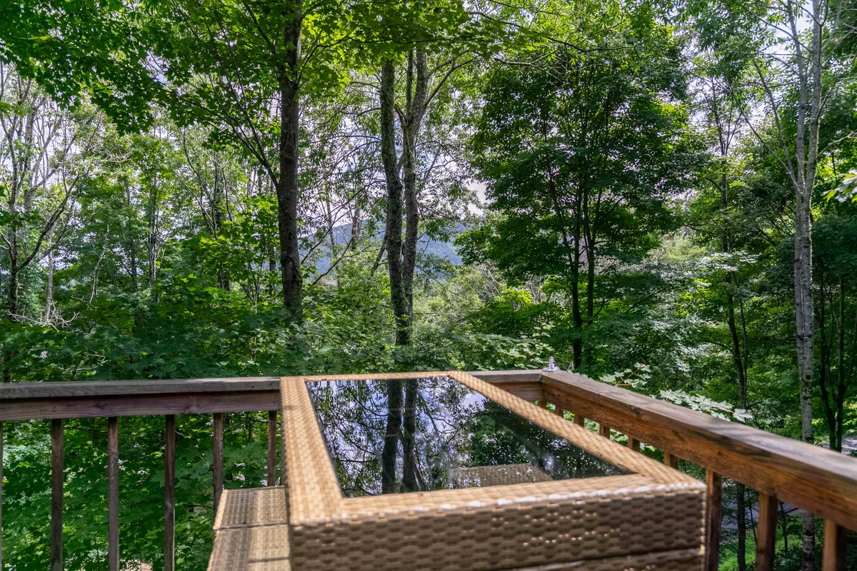 A peaceful view from a wooden deck, featuring a glass-top table and lush greenery just beyond the railing. The inviting outdoor space suggests a perfect spot to relax, watch wildlife, or unwind after a day outdoors.