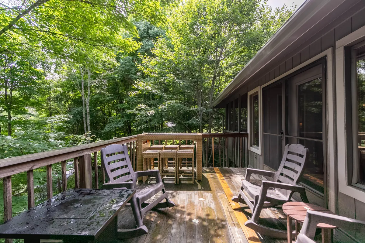 A spacious wooden deck nestled among lush greenery, furnished with comfortable outdoor seating. The setting is ideal for relaxing with morning coffee or gathering for evening conversations, with ample space suggesting privacy and tranquility. The peaceful atmosphere is enhanced by the surrounding foliage and the suggestion of expansive views.