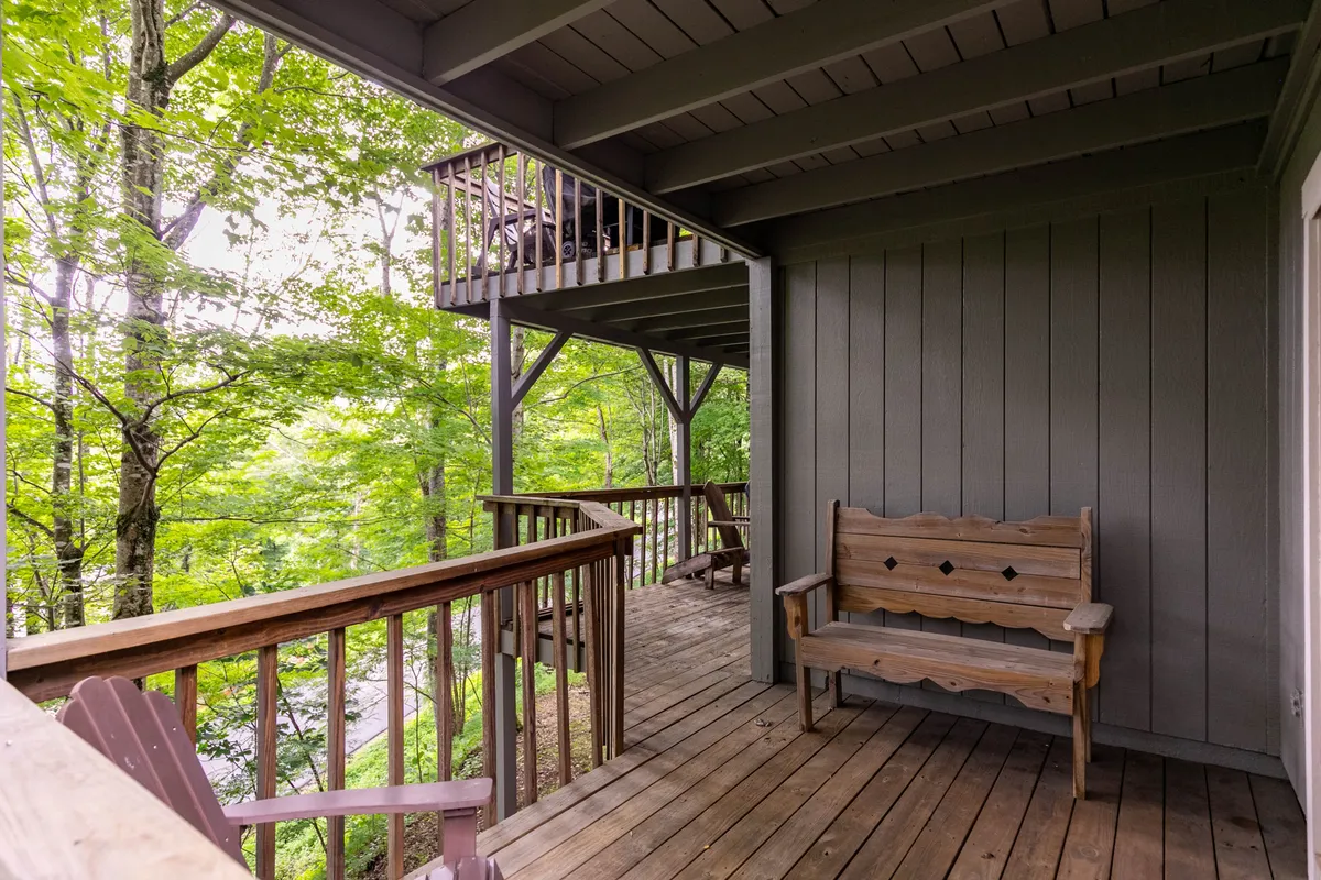 A quiet wooden bench on a deck, set against a backdrop of tall trees and a sturdy railing. The tranquil setting suggests a private nook for personal reflection, reading, or peacefully observing the changing seasons.