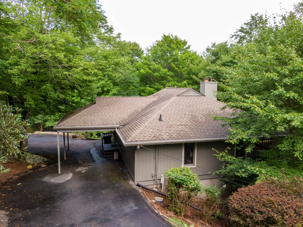 A peaceful, welcoming exterior shot of the house, showing its setting among the trees with a driveway leading up to the front. The image conveys the sense of arrival and hints at the adventure of driving up a mountain road in winter.