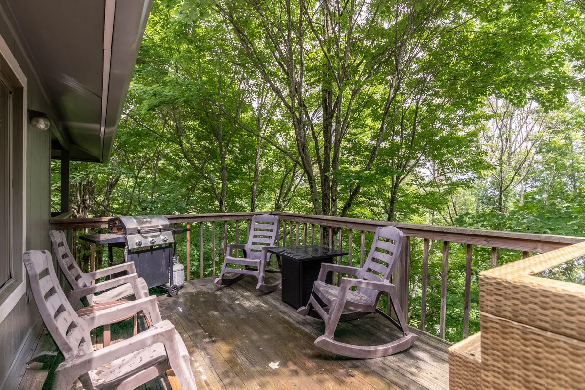 An inviting outdoor area with rocking chairs and a grill set on a covered porch, surrounded by lush greenery. This comfortable space is designed for relaxing after a day of adventure, stargazing, sharing stories, or enjoying a hot drink by the fire pit.