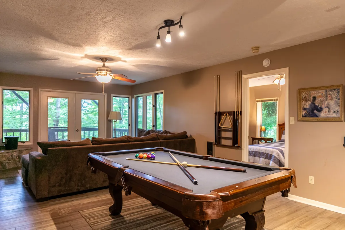 A friendly, casual lounge area featuring a pool table, a comfortable sofa, and large windows. The layout encourages both relaxed socializing and spirited pool competitions, with plenty of space for everyone to spread out.